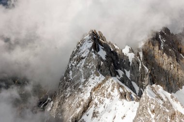 Görkemli bir dağ zirvesi bulutlardan oluşan bir battaniyeyi delip geçiyor.