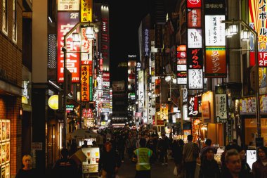 TOKYO, JAPONYAN - 22 Ekim 2024: Canlı ve hayat dolu bir şehir caddesi, neon ışıklarıyla aydınlanıyor ve geceleri kalabalıkla dolup taşıyor.