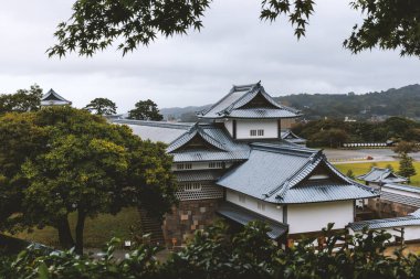 Yeşillik ve bulutlu gökyüzü ile çevrili geleneksel Japon kalesi, Kanazawa