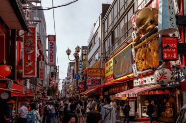 OSAKA, Japonya - 25 Ekim 2024: Asyalı bir metropolde çeşitli dükkanlar, meşgul insanlar ve renkli işaretlerle dolu canlı, canlı bir Osaka caddesi