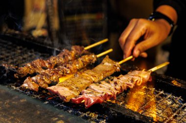 Cızırdayan et şişleri açık alevlerin üzerinde ızgara yapıyor, canlı bir gece pazarında aşçılık lezzetleri sergiliyor..
