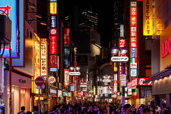 Токио, Япония - 3 ноября 2024 года: оживленная уличная сцена, освещенная красочными неоновыми вывесками, заполненная разнообразными людьми ночью