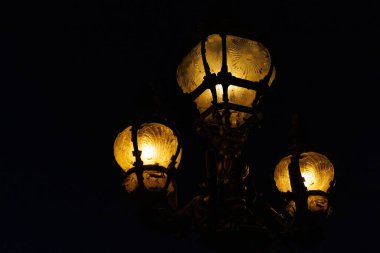 Karanlıkta üç ışığı olan bir lamba yanıyor. Işık sıcak ve davetkar.