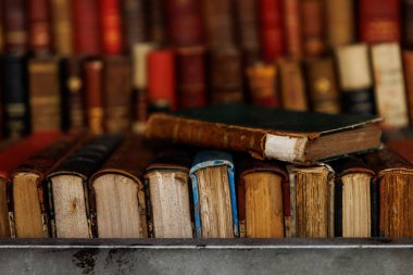 Üstünde yeşil bir kitap olan bir yığın kitap. Kitaplar eski ve eskimiş.