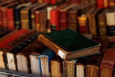 Üstünde yeşil bir kitap olan bir yığın kitap. Kitaplar eski ve eskimiş.