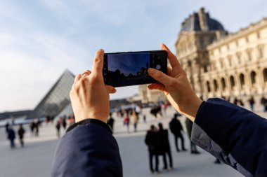 Bir kişi, arka planda bir grup insanla büyük bir binanın fotoğrafını çekiyor.