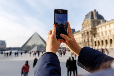 Bir kadın, arka planda bir grup insanla büyük bir binanın fotoğrafını çekiyor.