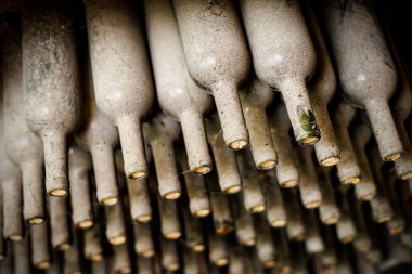 Bodrumda birbiri üstüne tozlu şarap şişeleri uzanıyor.