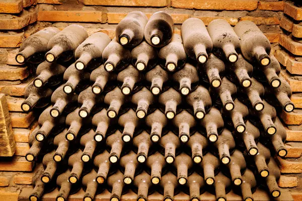 Bodrumda birbiri üstüne tozlu şarap şişeleri uzanıyor.