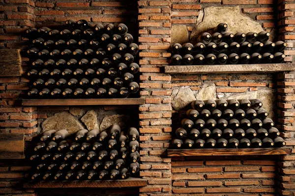 Ahşap ve tuğladan yapılmış raflarda dizilmiş şarap şişeleri koleksiyonu.