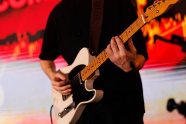 Bir adam sahnede elektro gitar çalıyor..