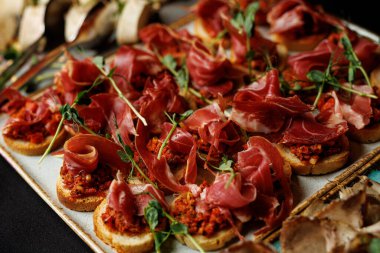 Yeşil garnitürlü bir tepsi et ve sebze. Et dilimlenir ve beyaz bir tabakta sıralanır.