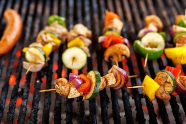 Assorted vegetable skewers grilling on barbecue. Includes zucchini, bell peppers, mushrooms and onions.
