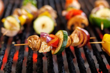 Vegetarian skewers with mushrooms, zucchini, onion, and peppers on a grill. Fresh vegetables roasting over open flames.