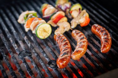 Sausages and chicken vegetable skewers on hot barbecue grill. Mixed meat being cooked over glowing coals outdoors.