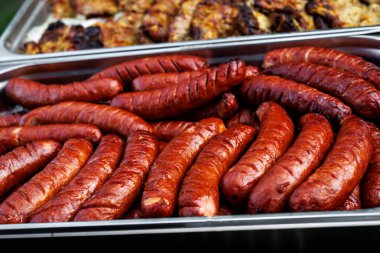 Close-up of grilled pork sausages arranged in a stainless steel tray. Juicy, golden-brown sausages served at an outdoor barbecue or catering event.
