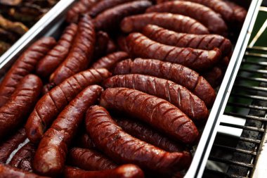 Close-up of juicy grilled sausages stacked in a serving tray. Outdoor food catering setup.