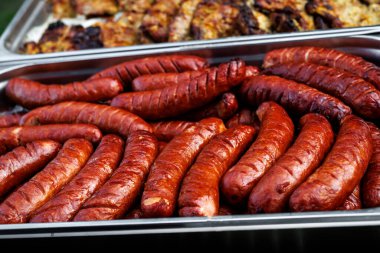 Close-up of grilled pork sausages arranged in a stainless steel tray. Juicy, golden-brown sausages served at an outdoor barbecue or catering event.