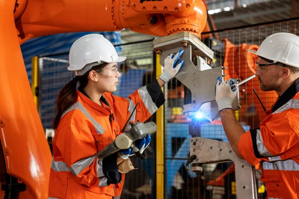 Asian male engineer and female programmer examining the operation of a smart industrial robotic arm for digital factory manufacturing technology.