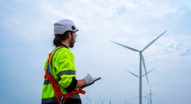 Male engineer in uniform looking at wind turbines in a windmill field