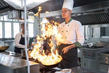 Asian male chef stir-frying vegetables over a blazing fire for Chinese stir-fry fresh vegetables in a restaurant
