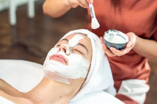 Beautiful young caucasian woman relaxing in hand spa, facial massage therapist doing facial massage to feel relaxed, moisturize facial skin, reduce wrinkles in wellness spa.
