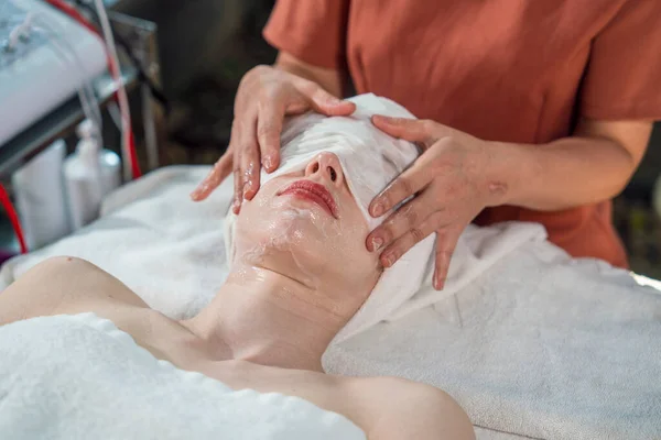Young beautiful caucasian lying at spa facial masseuse hands using cold cloth to close eyes to close pores, reduce wrinkles, help fresh skin, moisturize in spa wellness