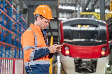 Kadın mühendis ve erkek teknisyen, üniformalı bakım ekibi ve güvenlik kaskı elinde tablet elektrik tren kontrol istasyonundaki elektrik tren tamir listesine bakıyor..