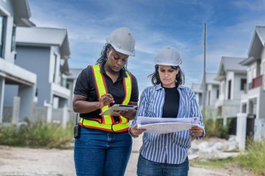 Kadın mimar elinde pano tutarken inşaat, inşaat, emlak konsepti gibi yeni inşaat alanındaki inşaat alanında kadın mühendis ile yeni projeyi tartışıyor.