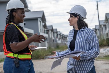 Kadın Afro-Amerikan mühendis ve erkek mühendis inşaat alanındaki planlar hakkında konuşuyorlar. İnşaat mühendisi ve kadın inşaat alanında çalışıyor.