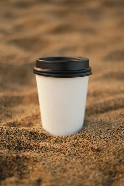 mockup of a disposable white cup of coffee to go on the beach close-up