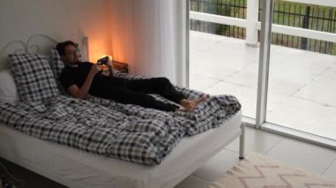 a man lies on a bed and reads the news in a smartphone