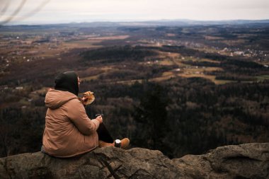 woman tourist on the top of the mountain enjoys the view and eats a sandwich