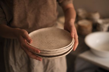 Çömlek atölyesindeki kadın seramik kovmak için tabak taşıyor.