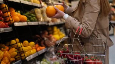 Bir kadın süpermarkette portakal seçer ve onları sepetine koyar.