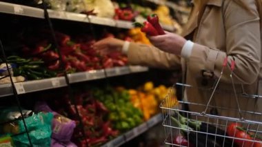 Tezgahın yanında sebzeli genç bir kadın tatlı biber seçiyor ve sepete koyuyor.