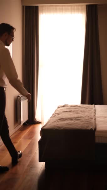 古典的なスーツケースを着た若い男がスーツケースを持って寝室に入りベッドの上に横になって — ストック動画