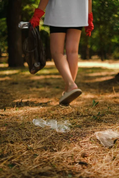 a woman in gloves walks in the park and collects plastic in a trash bag