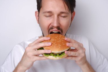 Beyaz arka planda hamburger yiyen beyaz bir adamın portresi.