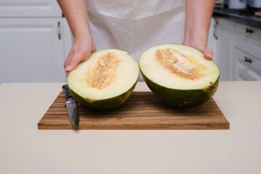 Mutfakta bir aşçı olgun bir kavunu yakın planda keser.