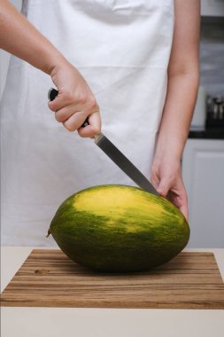Mutfakta bir aşçı olgun bir kavunu yakın planda keser.