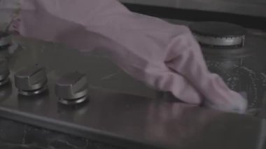 Koruyucu eldivenler giymiş, temizlik ürünü video kayıt cihazıyla gaz sobasını yıkayan kadınların yakın plan fotoğrafları.