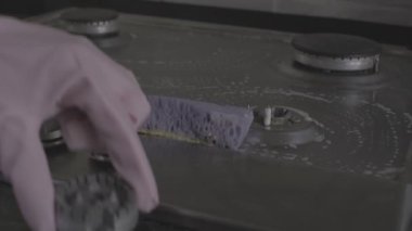 Koruyucu eldivenler giymiş, temizlik ürünü video kayıt cihazıyla gaz sobasını yıkayan kadınların yakın plan fotoğrafları.