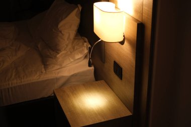 Modern bir otel odasındaki yatağın üstünde gece lambası.
