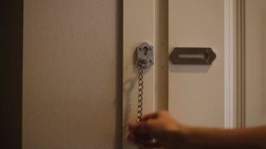 Bir adam ön kapıyı zincirle kapatır.