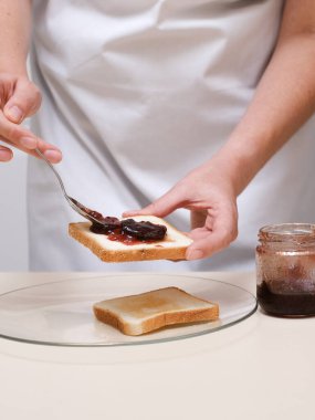 Genç bir kadın tostun üzerine reçel sürüyor.
