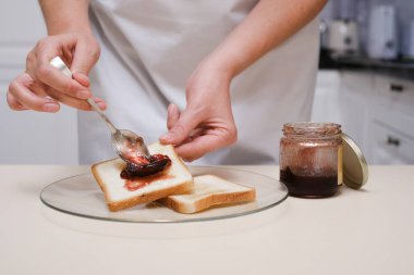 Genç bir kadın tostun üzerine reçel sürüyor.