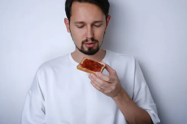 白い背景にジャムでトーストを食べる若いブルネット男の肖像画 ストックフォト