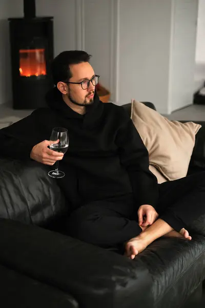 若い男は暖炉のある田舎の家に座って 山を見ながらワインを飲む ロイヤリティフリーのストック画像