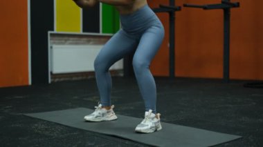 Güzel kaslı sporcu kadın paspasın üzerinde spor salonunda çömeliyor.
